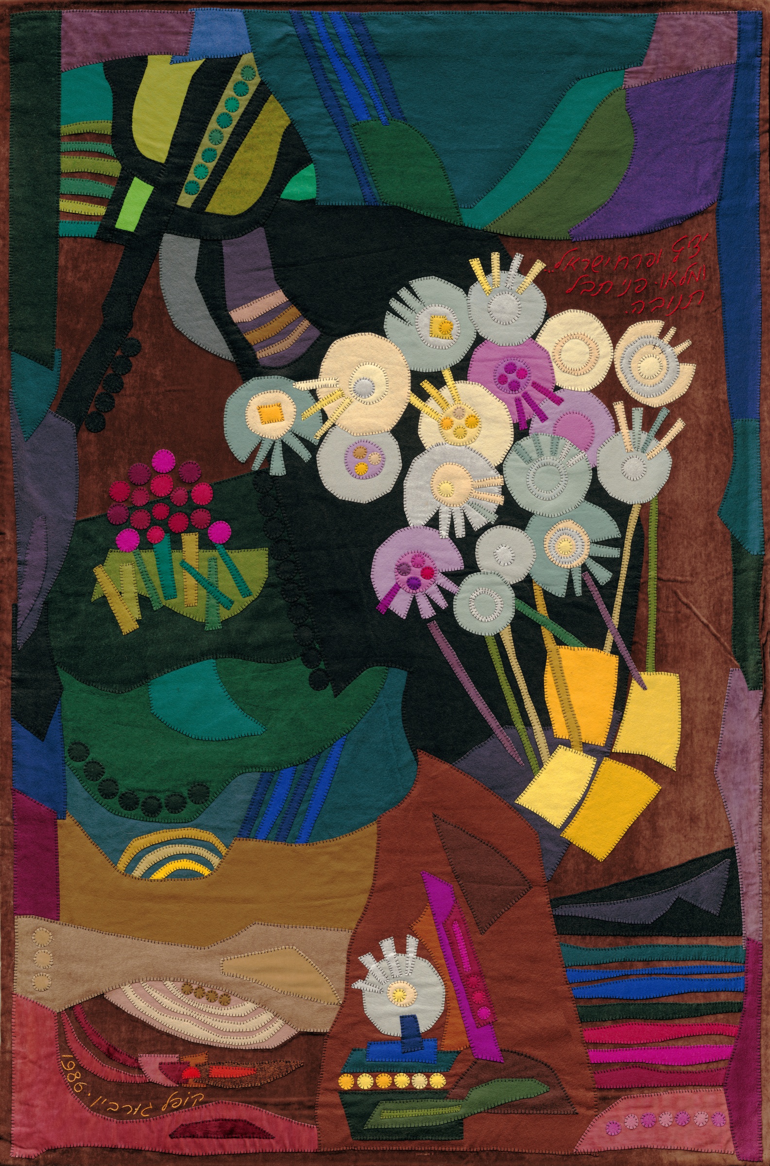 Fruitage by Kopel Gurwin, an abstract hand-cut felt appliqué composed of overlapping geometric and organic forms in turquoise, green, purple, ochre, and terracotta. Clusters of circular flowers in white, pink, and pale blue rise through the composition, accompanied by a handwritten Hebrew inscription in the upper right.