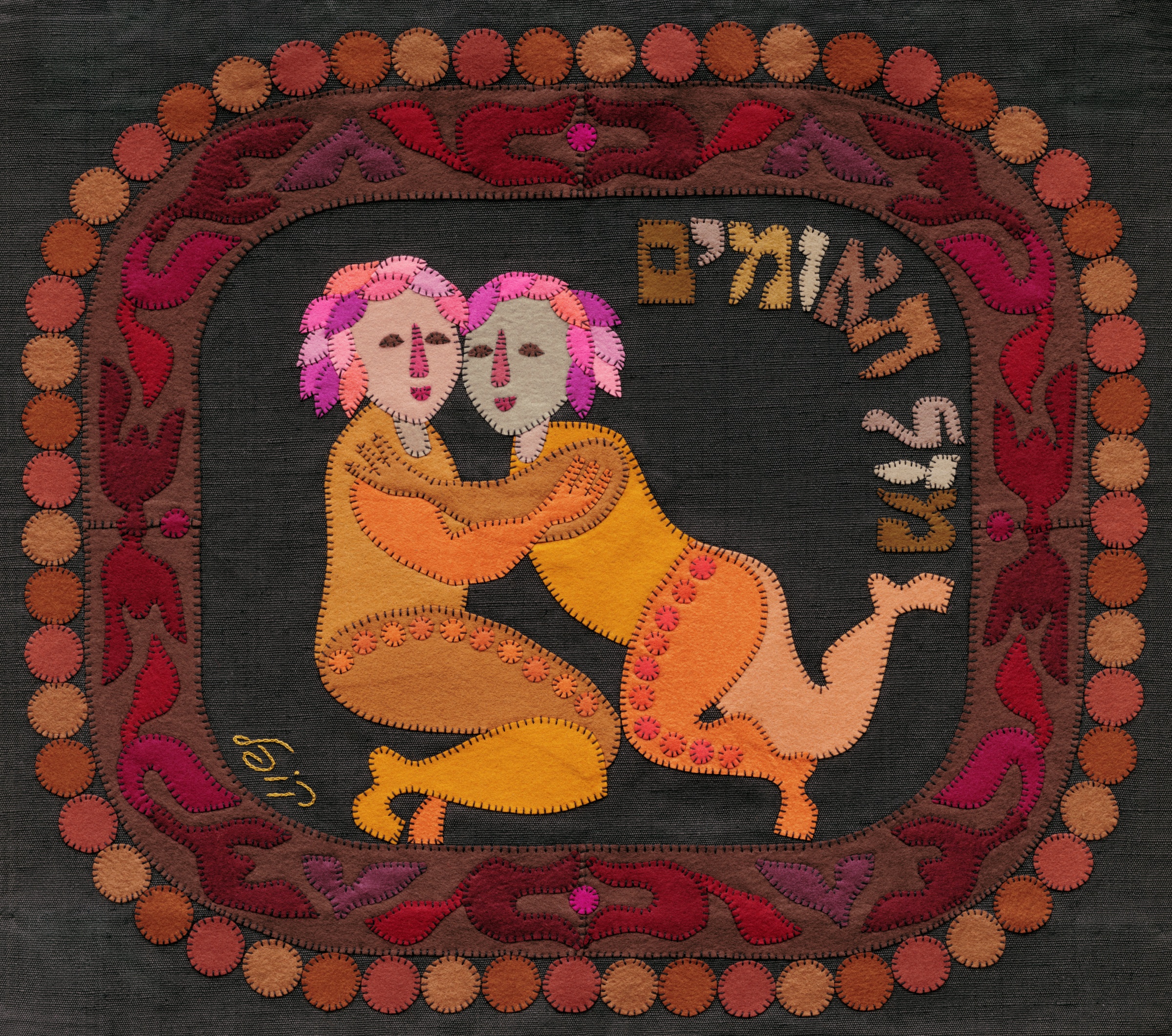 Gemini by Kopel Gurwin, a hand-cut felt appliqué depicting two embracing twin figures in warm golden and peach tones, framed by a reddish ornamental border with circular motifs and a Hebrew zodiac inscription.