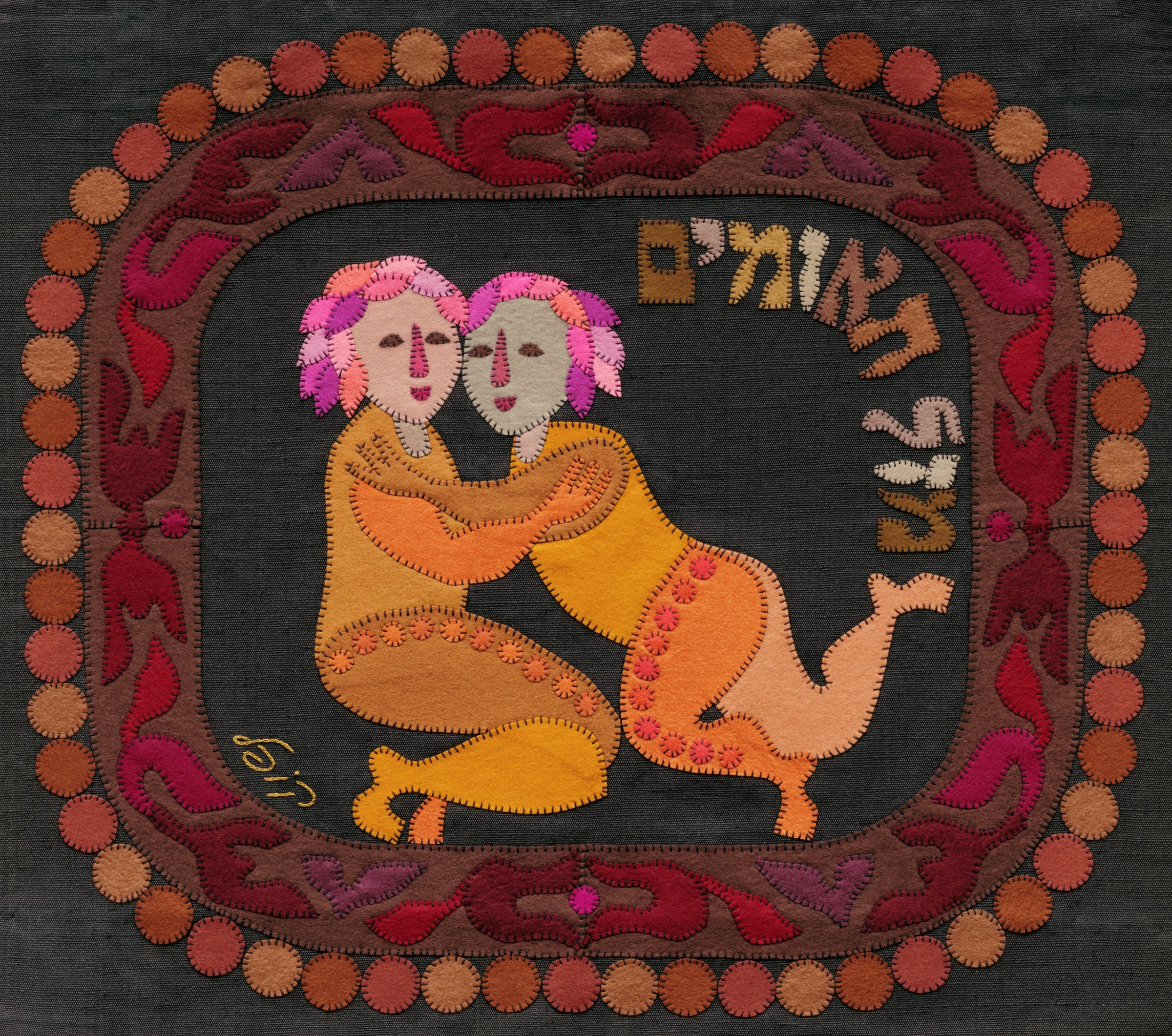 Gemini by Kopel Gurwin, a hand-cut felt appliqué depicting two embracing twin figures in warm golden and peach tones, framed by a reddish ornamental border with circular motifs and a Hebrew zodiac inscription.