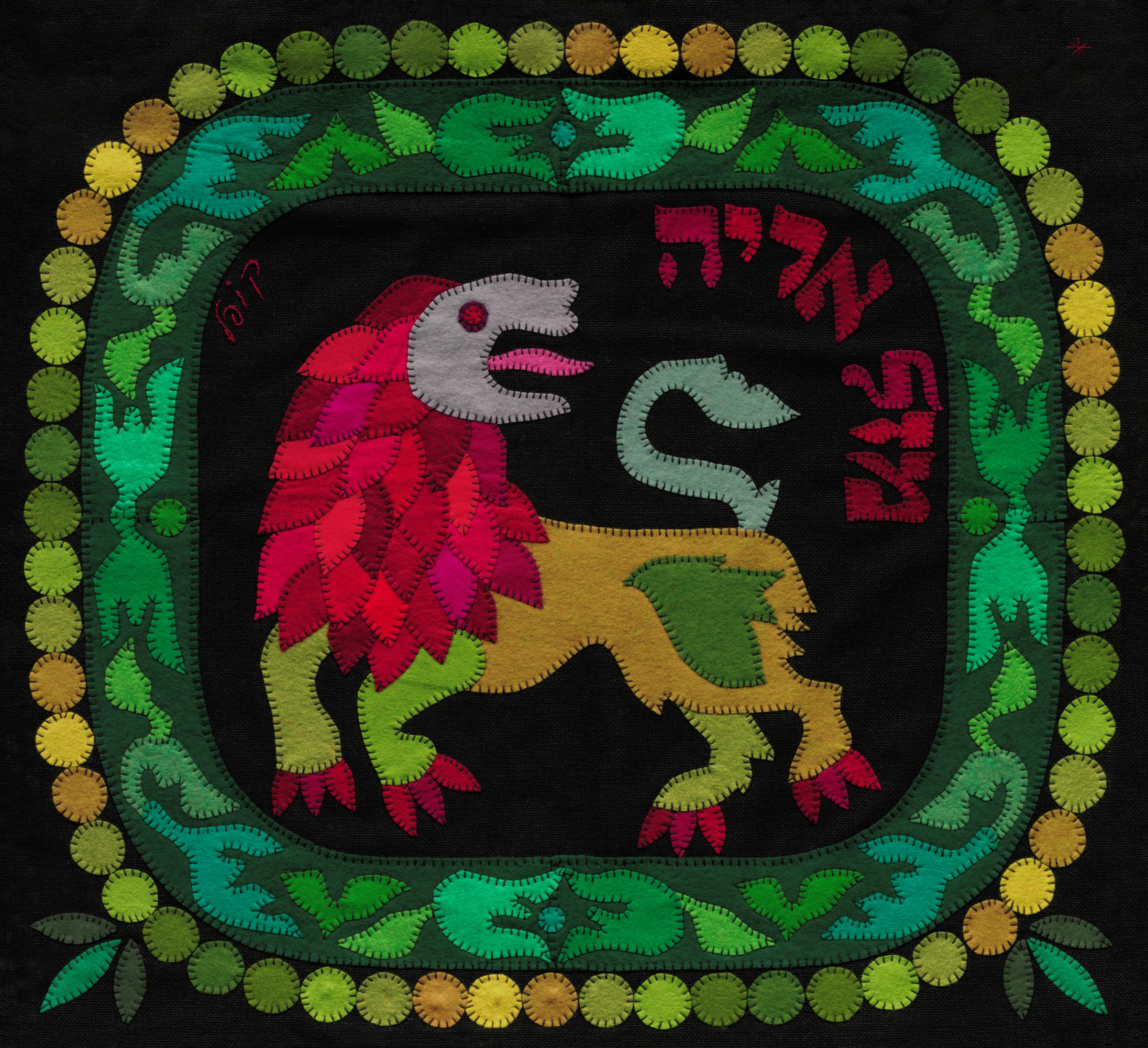Leo by Kopel Gurwin, a hand-cut felt appliqué depicting a stylized lion with a red and magenta mane, a yellow and green body, and an upturned tail. The lion stands against a black background, surrounded by an ornate green, turquoise, and purple border edged with yellow and green circles. Red Hebrew lettering identifies the sign as Mazal Arye.