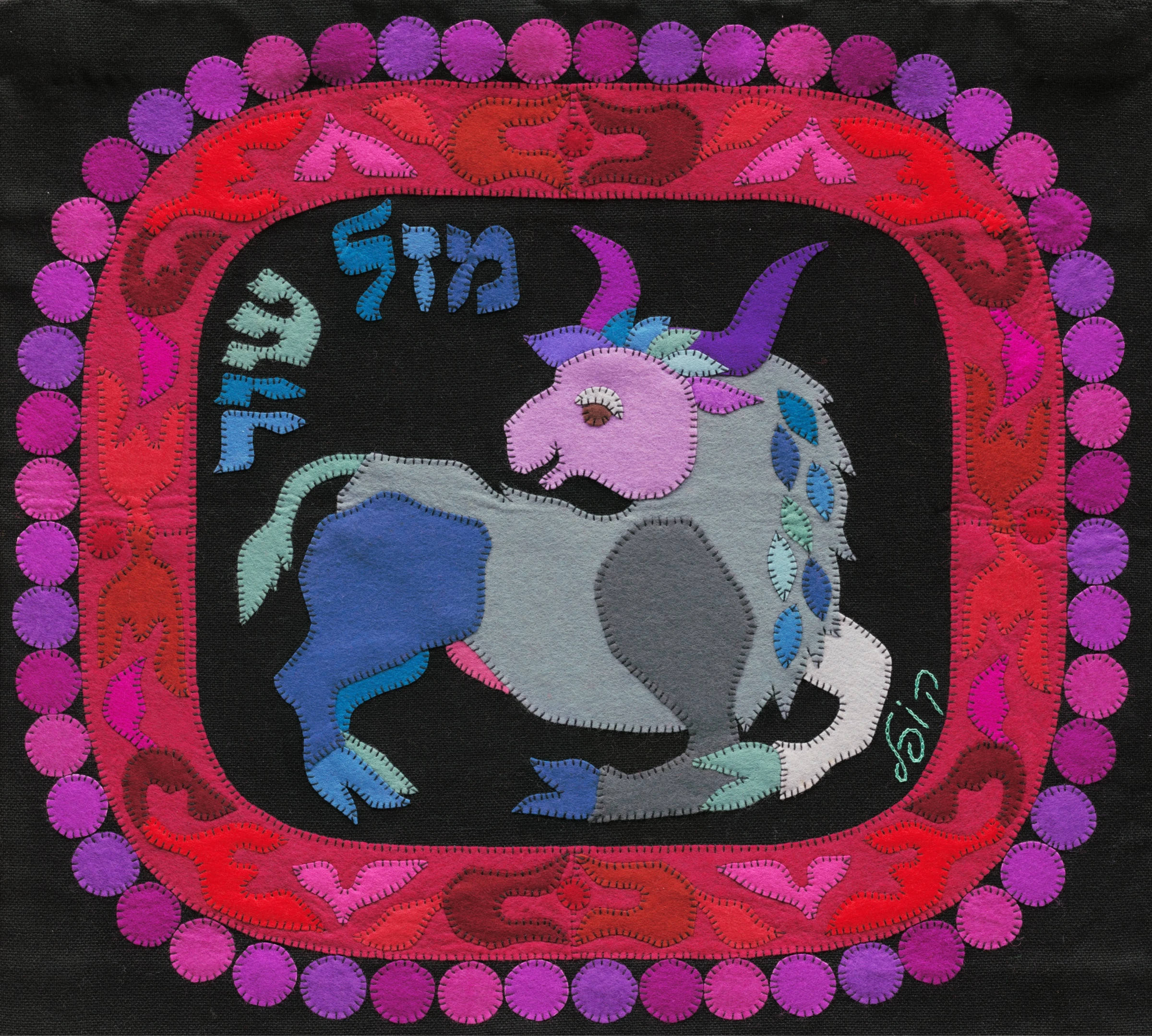 Taurus by Kopel Gurwin, a hand-cut felt appliqué depicting a stylized bull in pale grey, blue, and lavender against a deep black background, framed by a vivid ornamental border in red, pink, and purple tones. Hebrew lettering identifies the zodiac sign as Mazal Shor.